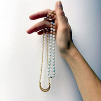 A hand holds a Mala made of Citrine, peach Moonstone and Aquamarine beads with a gold plated Crescent Moon pendant.