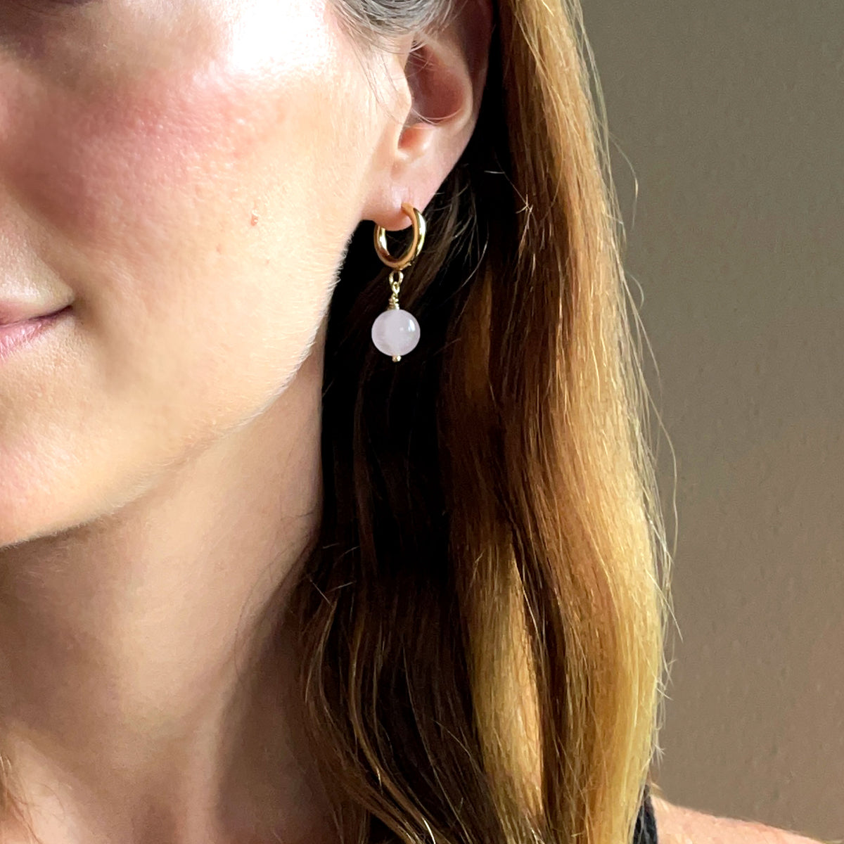 A woman wears a pair of gold plated  huggie hoops with a 10mm round Rose Quartz bead.