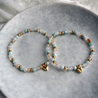 Pair of Sisterhood Bracelets made of citrine, rose quartz, amazonite, and golden spacer beads with heart charm, styled on ceramic plate.