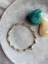 Sisterhood Bracelet with citrine, rose quartz, amazonite beads, and gold heart charm displayed with matching gemstones on plate.