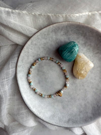 Delicate Sisterhood Bracelet featuring citrine, rose quartz, amazonite, and gold-filled accents with heart charm, styled with crystals and linen fabric.