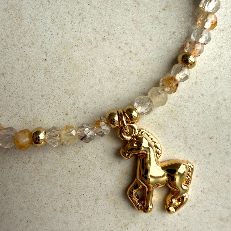 Close-up of gold horse charm on a handmade topaz gemstone bead bracelet with gold-filled accents on ceramic background – Year of the Horse jewelry by Moksha Jewelry.