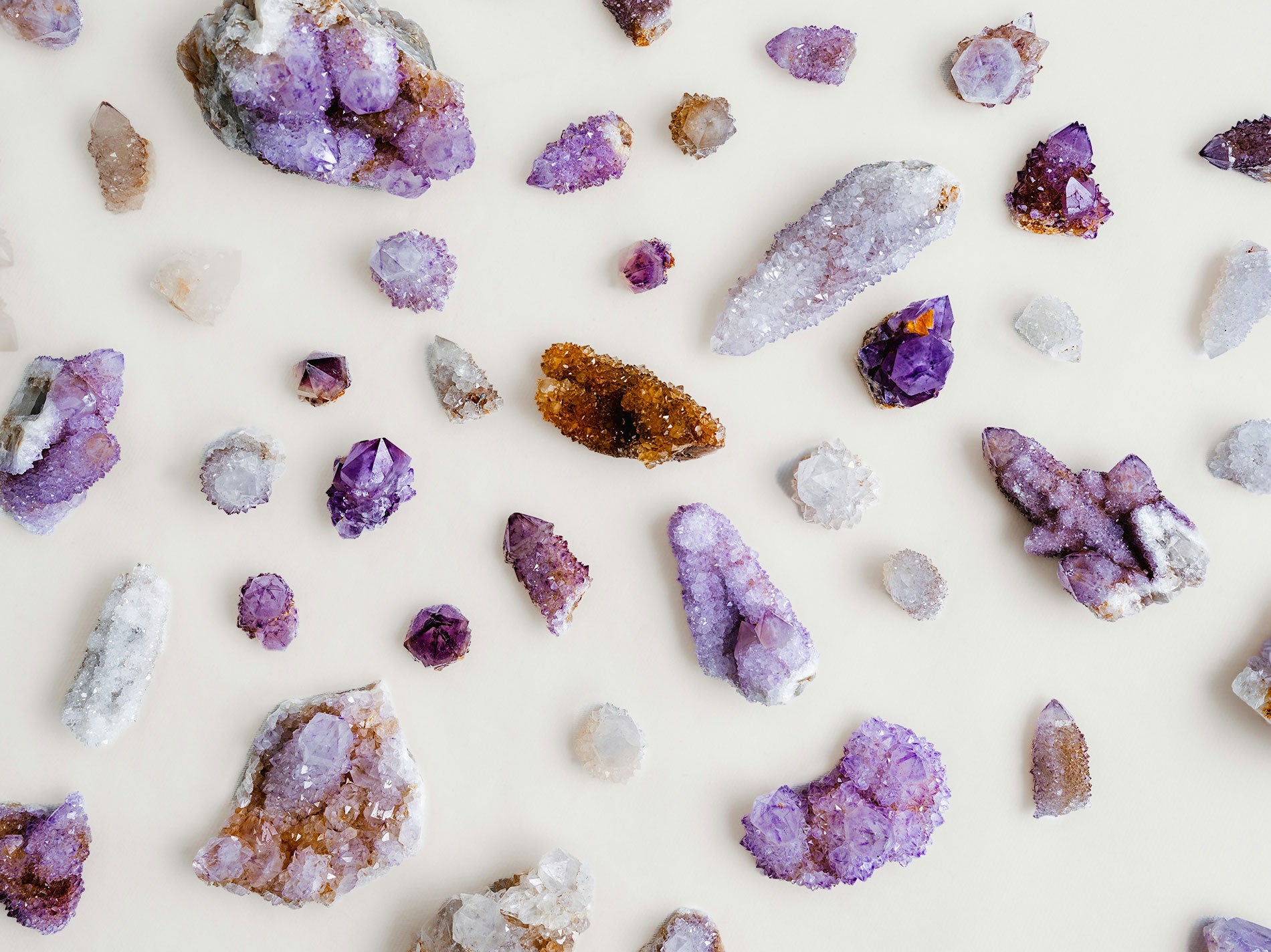 A variant of different raw gemstones in hues from white to purple on a white background.